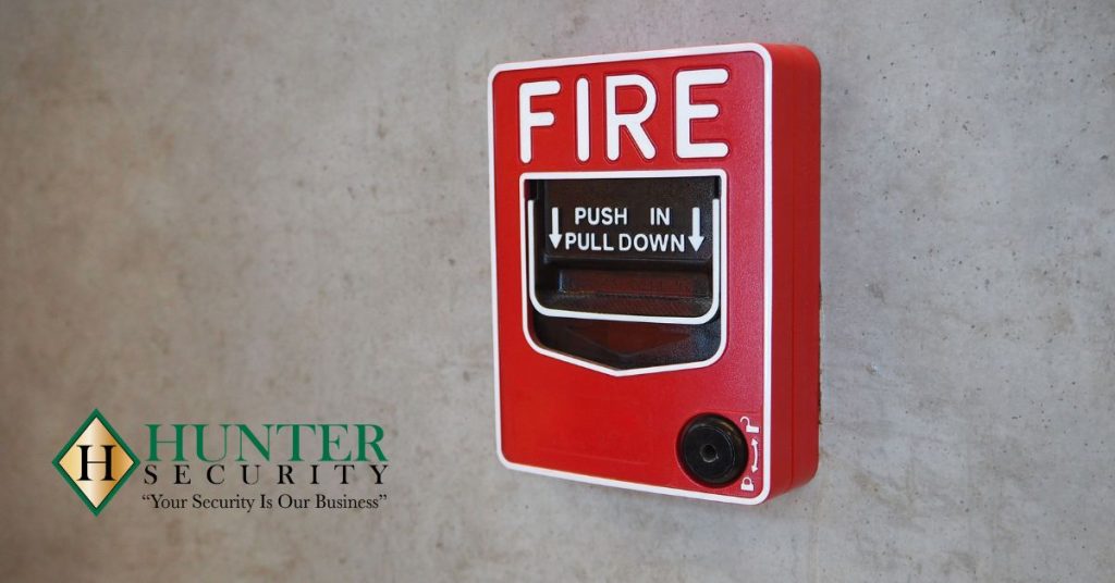 Red manual fire alarm pull station mounted on a concrete wall with Hunter Security logo