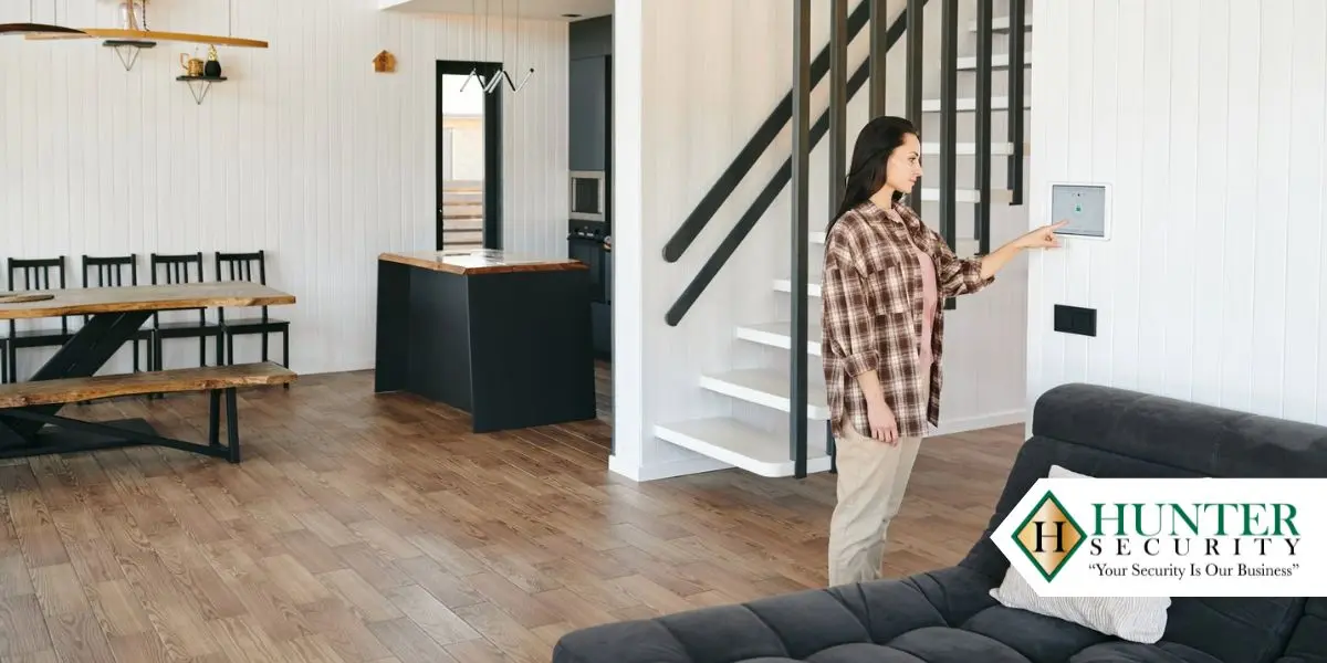 Woman arming a wall-mounted smart security panel in a modern open-plan Alabama home