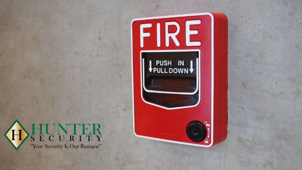 Red manual fire alarm pull station mounted on a concrete wall with Hunter Security logo